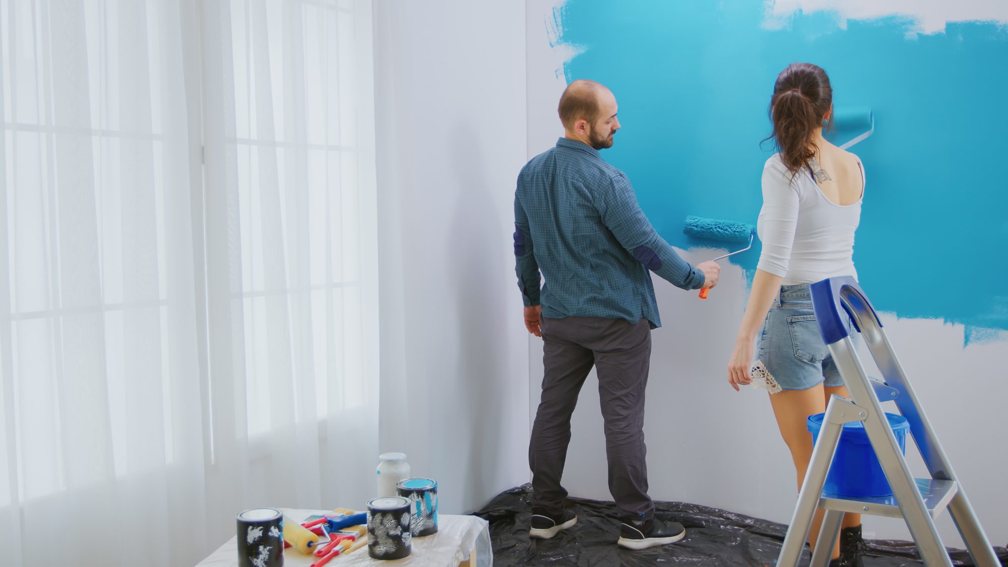 caucasian couple painting wall with roller brush blue paint apartment redecoration home construction while renovating improving repair decorating